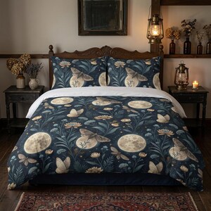 May include: A dark blue duvet cover and two matching pillowcases featuring a repeating pattern of beige moths, full moons, and floral botanical elements. The bedding set is displayed on a wooden bed frame with a white flat sheet visible at the top.