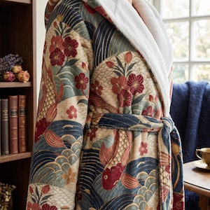 Puede incluir: Bata de felpa con un colorido estampado de peces koi y flores en tonos rojos, azules y beige. La bata presenta un cuello blanco y esponjoso y un cinturón a juego. El diseño incluye olas y flores estilizadas.