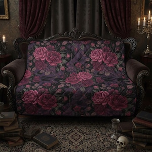 May include: A quilted throw blanket featuring a dark purple backdrop adorned with large, pink roses. The blanket is draped over a dark brown sofa with intricate carvings. The overall style is gothic and romantic, suitable for a vintage interior.