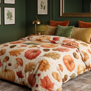 Puede incluir: Una funda nórdica y fundas de almohada de color crema con un patrón repetitivo de calabazas naranjas, bellotas marrones y hojas de otoño multicolores en tonos rojos, naranjas y amarillos sobre la superficie de la tela.