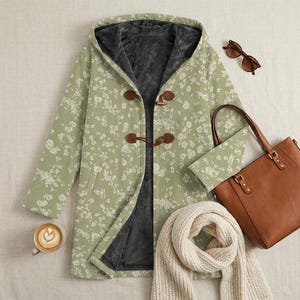 May include: A sage green hooded coat with a white floral pattern, dark gray fleece lining, and brown toggle closures. Accompanied by a brown leather tote bag, a cream-colored knit scarf, a pair of brown sunglasses, and a ceramic mug of latte.