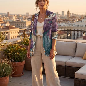May include: A blazer featuring a vibrant floral pattern in shades of purple, teal, and orange, worn over a cream-colored camisole and paired with high-waisted, wide-leg beige trousers. The blazer has a single button closure and notched lapels.
