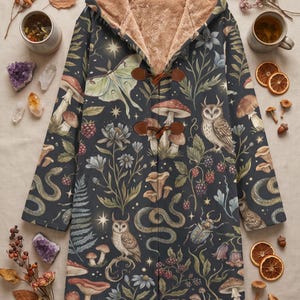 May include: A dark-coloured hooded coat with a tan faux-fur lining, featuring a repeating pattern of owls, snakes, moths, mushrooms, berries, and stars. The coat has two brown toggle closures on the front and long sleeves with a straight hemline.