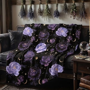 May include: A black throw blanket featuring a repeating pattern of purple peony flowers, golden crescent moons, and small sparkling stars. The fabric displays a soft texture with a dark background that highlights the floral and celestial motifs.