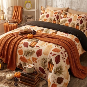 Pode incluir: Um conjunto de cama com capa de edredão e fronhas em tom creme com um padrão de folhas de outono, ramos de pinheiro, lanternas e velas. Um lençol preto liso e uma manta texturizada em tom laranja queimado estão dispostos sobre a cama.
