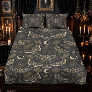 May include: Dark grey quilt set featuring a repeating pattern of moths, moons, suns, and foliage in a light tan colour. The set includes a quilt and two pillow shams, all with a quilted design. The bedding is on a dark wooden bed frame.