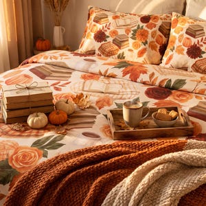 Op de afbeelding: Een beddengoedset met een crèmekleurig dekbedovertrek en twee bijpassende kussenslopen, versierd met een patroon van herfstbladeren, oranje bloemen, stapels boeken en kleine pompoenen, aangevuld met een dikke, getextureerde deken in roestoranje.