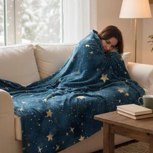 May include: A deep blue plush throw blanket featuring a repeating pattern of gold-colored stars in various sizes and small white dots scattered across the fabric. The blanket has a soft, fuzzy texture and is draped over a white sofa.