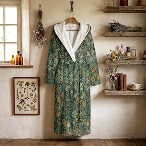 May include: A long-sleeved hooded robe featuring a dark green base with a repeating botanical pattern of orange, yellow, and light green flowers and leaves. The robe includes a white plush interior lining, a hood, and a matching fabric waist tie.
