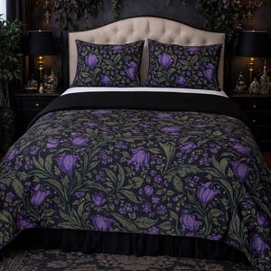 May include: A bed dressed with a duvet cover and two pillowcases featuring a dark floral pattern of purple flowers and green leaves on a black backdrop. The bed has a black valance and is set against a dark wall.