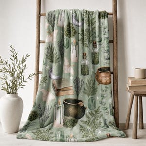 May include: A soft sage green throw blanket featuring a repeating pattern of botanical elements, including ferns, lavender, and eucalyptus, alongside illustrations of crescent moons, moths, candles, glass apothecary bottles, and a dark cauldron.