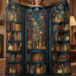 May include: A dark blue throw blanket with a detailed illustration of a bookshelf filled with books, bottles, and flowers. The design has a vintage aesthetic with gold and brown tones, creating a cosy and whimsical feel. The blanket is held up by a person.