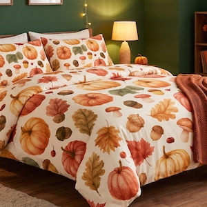 Puede incluir: Un juego de cama que incluye una funda nórdica y dos fundas de almohada de color crema con un patrón de acuarela repetitivo de calabazas naranjas, bellotas marrones y hojas de otoño multicolores, junto con una manta de color naranja quemado.