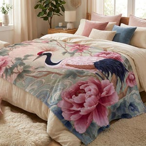 Può includere: Una morbida coperta decorata con una grande illustrazione dettagliata di una gru della Manciuria tra peonie rosa vivaci e fogliame verde. Il disegno è posto su uno sfondo dai toni chiari e neutri con delicate sfumature di colore blu.
