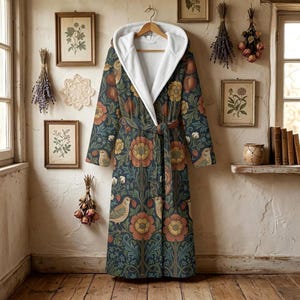 May include: A long-sleeved hooded robe featuring a dark blue background with a repeating pattern of orange flowers, pomegranates, and birds. The robe includes a white fleece-lined hood, a matching fabric tie belt at the waist, and long sleeves.