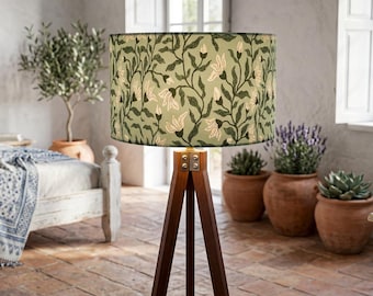 May include: A floor lamp with a tripod base made of dark wood and a cylindrical lampshade featuring a sage green background with a repeating pattern of dark green vines and light-colored floral buds.