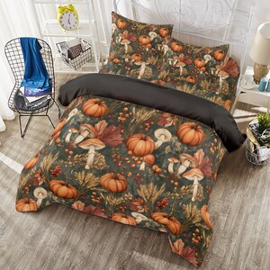 Puede incluir: Un juego de cama con fondo verde oscuro y un patrón repetitivo de calabazas naranjas, varios hongos, tallos de trigo y hojas de otoño. La funda nórdica tiene una sección superior negra sólida e incluye dos fundas de almohada a juego.