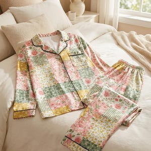May include: A two-piece pyjama set featuring a long-sleeved button-down shirt and matching trousers. The fabric displays a patchwork design of floral patterns in shades of pink, yellow, and green, accented with thin black piping along the collar.