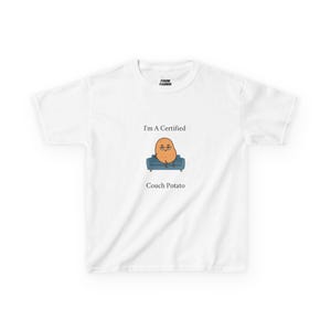 Puede incluir: Camiseta blanca con el texto "I'm A Certified Couch Potato" y un personaje de dibujos animados de patata sentado en un sofá azul. La camiseta tiene cuello redondo y mangas cortas.