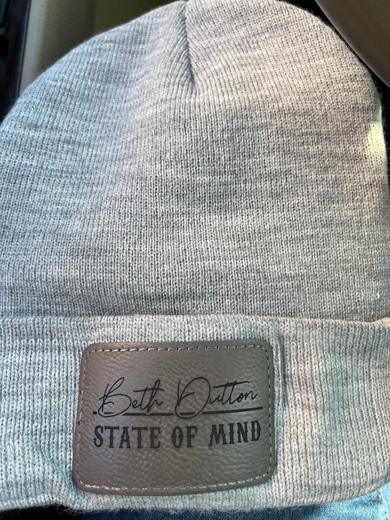May include: Gray beanie with a brown leather patch that says "Beth Dutton State of Mind" in black lettering.