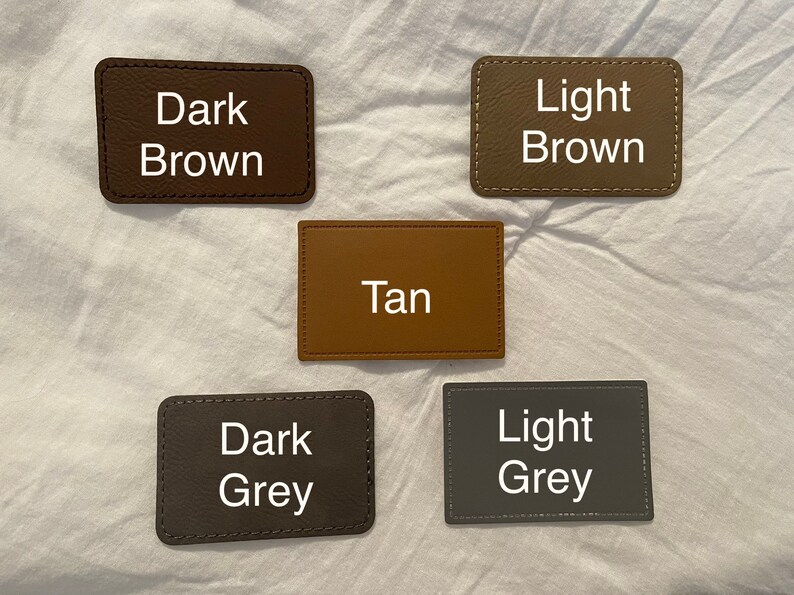 May include: Five leather swatches in different colors: dark brown, light brown, tan, dark grey, and light grey. Each swatch has the color name written in white text.