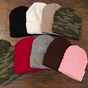 May include: Assortment of ten beanies in various colors and patterns, including black, white, brown, pink, red, gray, and camouflage. Some beanies have a pom-pom on top.