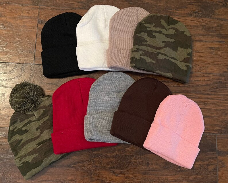May include: Assortment of ten beanies in various colors and patterns, including black, white, brown, pink, red, gray, and camouflage. Some beanies have a pom-pom on top.