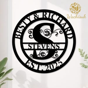 Może przedstawiać: Czarny metalowy znak z nazwiskiem rodziny z imionami "Besty & Richard" i "Stevens" ze środkową literą "S". Znak zawiera również "EST. 2025" i dekoracyjne kwiatowe akcenty. Znak jest okrągły.