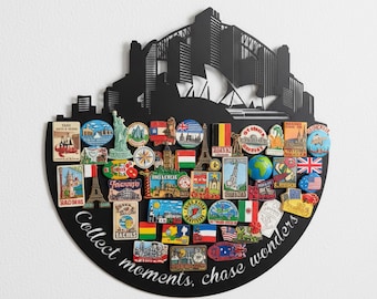 May include: Black metal wall art in a half-circle shape, featuring a cityscape silhouette and various travel-themed magnets. The magnets showcase landmarks and flags from around the world. The phrase "Collect moments, chase wonders" is written on the bottom.