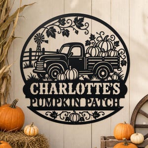 Könnte beinhalten: Ein rundes Wandbild aus schwarzem Metall mit einem Scherenschnitt-Design eines alten Pick-ups, der mit Kürbissen beladen ist. Die Szene zeigt eine Windmühle, einen Zaun und Ahornblätter. Der Text "CHARLOTTE'S PUMPKIN PATCH" steht im unteren Bereich.