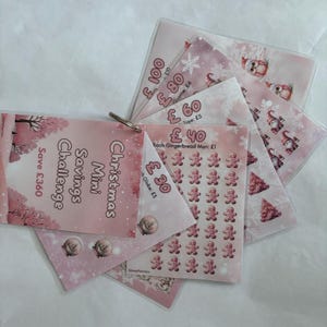 Op de afbeelding: Een roze en witte kerst spaaruitdaging met een totaal spaardoel van € 360. De uitdaging omvat een ​​verscheidenheid aan items om voor te sparen, waaronder een gnome, een boom, peperkoekmannetjes en een sneeuwbol. Elk item heeft een prijs ernaast.