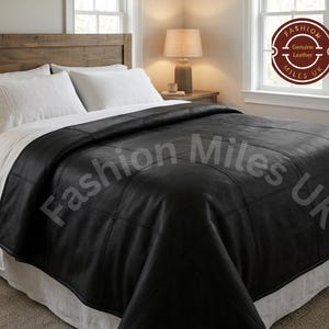 May include: A black leather bedspread featuring a grid-like stitched pattern. The bedspread is draped over a bed with white pillows and a white bed skirt. A circular logo in the corner reads Fashion Miles UK Genuine Leather.