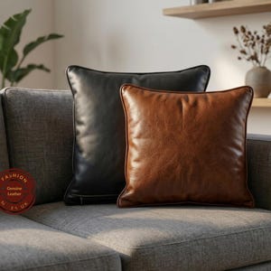 May include: Two square leather cushions on a grey sofa. One cushion is black, the other is brown. The cushions have a textured appearance and are placed against a neutral background.