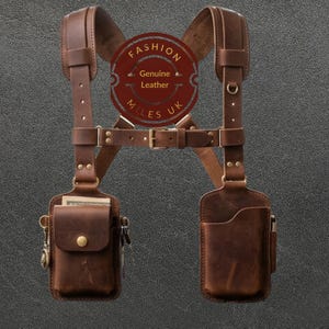 May include: A brown leather shoulder holster harness featuring two attached pouches, adjustable straps with metal buckles, and a circular logo patch with the text FASHION GENUINE LEATHER MILES UK. The harness includes brass-toned hardware and rivets.