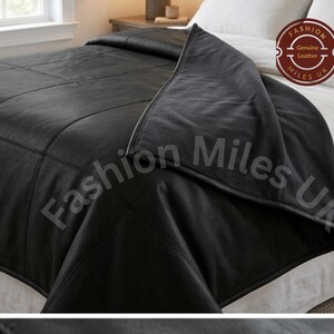 May include: A black leather bedspread featuring a grid-like stitched pattern and a smooth finish. The textile is draped over a white bed. A circular logo in the corner contains the text Fashion Miles UK and Genuine Leather.