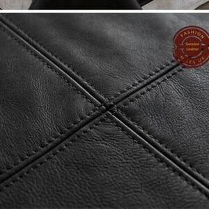 May include: A black leather surface with a textured grain and a cross-stitched pattern featuring double rows of stitching. A circular red stamp in the upper right corner contains the text FASHION, Genuine Leather, and M LES UK in white lettering.