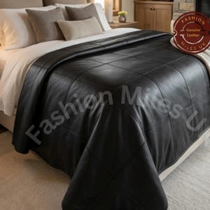 Puede incluir: Una colcha de cuero negro con un patrón de costuras en cuadrícula sobre una cama. Una insignia circular en la esquina superior derecha muestra el texto Fashion Genuine Leather Miles UK. La colcha cubre sábanas blancas y varias almohadas.