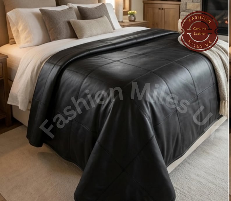 May include: A black leather bedspread featuring a grid-stitched pattern draped over a bed. A circular badge in the upper right corner displays the text Fashion Genuine Leather Miles UK. The bedspread covers white sheets and several neutral-toned pillows.