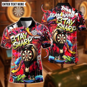 Könnte beinhalten: Ein kurzärmeliges Poloshirt mit einem Graffiti-Design. Das Shirt zeigt einen Cartoon-Dartscheiben-Charakter mit Sonnenbrille und roter Jacke. Der Text enthält "STAY SHARP" und "YOUR NAME". Der Hintergrund ist eine Mischung aus Rot, Schwarz und farbenfrohen Graffiti.