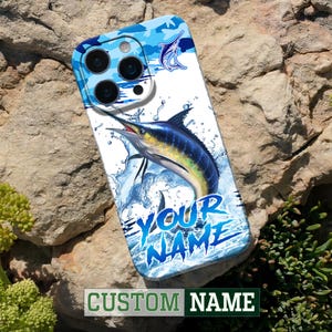 Puede incluir: Funda de teléfono personalizada con un marlín azul saltando del agua. El diseño incluye un patrón de camuflaje azul en la parte superior y el texto "YOUR NAME" en azul, con "CUSTOM NAME" en la parte inferior.