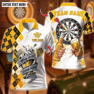 Pode incluir: Camisa polo branca com um padrão de losangos amarelos e pretos nas mangas. A camisa apresenta um design de dardo nas costas e um gráfico que diz "Play darts drink beer" na frente. O texto "ENTER TEXT HERE" está no topo.