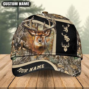 May include: A baseball cap featuring a camouflage pattern with a central deer head illustration. The design includes three smaller deer head silhouettes on a black side panel and the text CUSTOM NAME at the top and YOUR NAME on the brim.