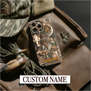 May include: A phone case with a camouflage design featuring a deer and skull illustration. The case has the text "YOUR NAME" and "CUSTOM NAME" on it. The case is surrounded by a hat, jacket, and other hunting-themed items.