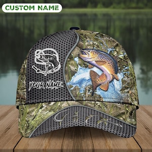 May include: A camouflage baseball cap featuring a leaping trout with water splash details. The cap includes the text "CUSTOM NAME" and "YOUR NAME" in white, along with a fish logo. The design incorporates shades of green, brown, and gray.