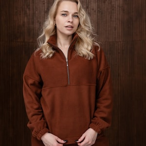 Può includere: Un pullover in pile color ruggine con collo alto e chiusura con zip a un quarto. I pantaloni in pile abbinati completano il comodo completo da casa. L'outfit è realizzato in materiale morbido e caldo.
