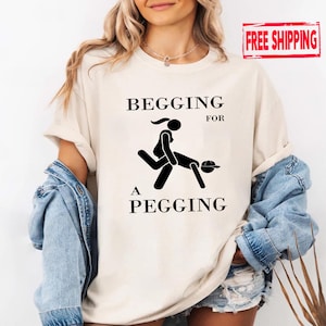 May include: Cream-colored t-shirt with the text "BEGGING FOR A PEGGING" in black, along with a stick figure graphic. The shirt is worn with a denim jacket and shorts. A "FREE SHIPPING" stamp is visible.