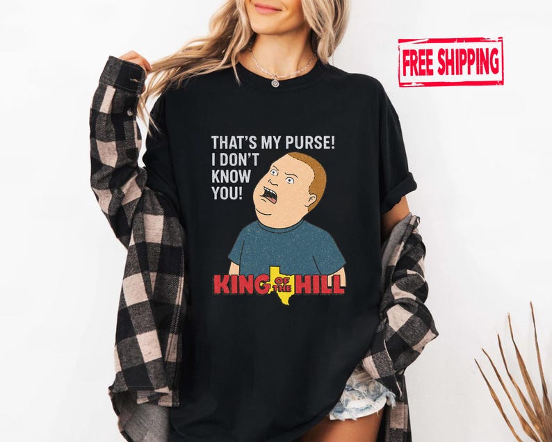 May include: Black t-shirt with a cartoon image of Bobby Hill from King of the Hill. The shirt has the text "THAT'S MY PURSE! I DON'T KNOW YOU!" above the character and "KING OF THE HILL" below.