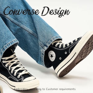 May include: Black high-top sneakers with white laces and a white sole. The sneakers have a classic design with a star logo on the side. The text "Converse Design" is at the top, and "Embroidery according to Customer requirements" is at the bottom.