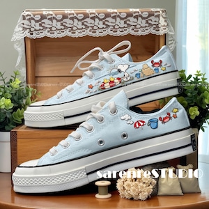 Peut inclure: Baskets en toile bleu clair avec lacets et semelles blanches. Les baskets présentent un motif sur le thème de la plage avec des personnages de dessins animés, dont Snoopy, sur les côtés. Les chaussures ont un design classique à coupe basse avec un embout en caoutchouc.