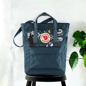 May include: A teal Fjallraven Kanken backpack with a custom embroidered design. The design features elements from Van Gogh's "Starry Night" and a logo. The bag has a front pocket, top handles, and adjustable shoulder straps.